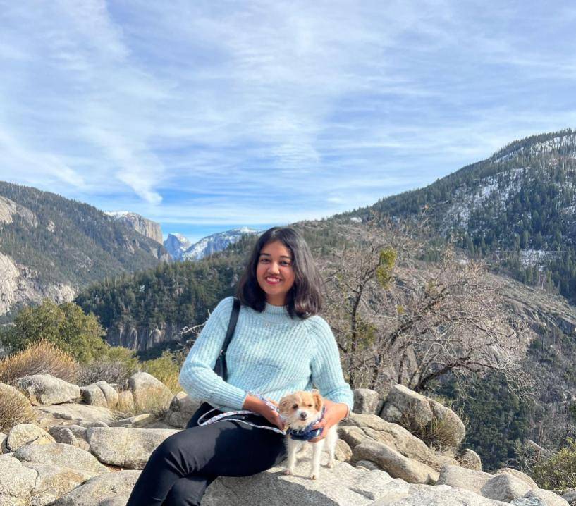 Woman sitting on rocks with a small dog and mountains behind her